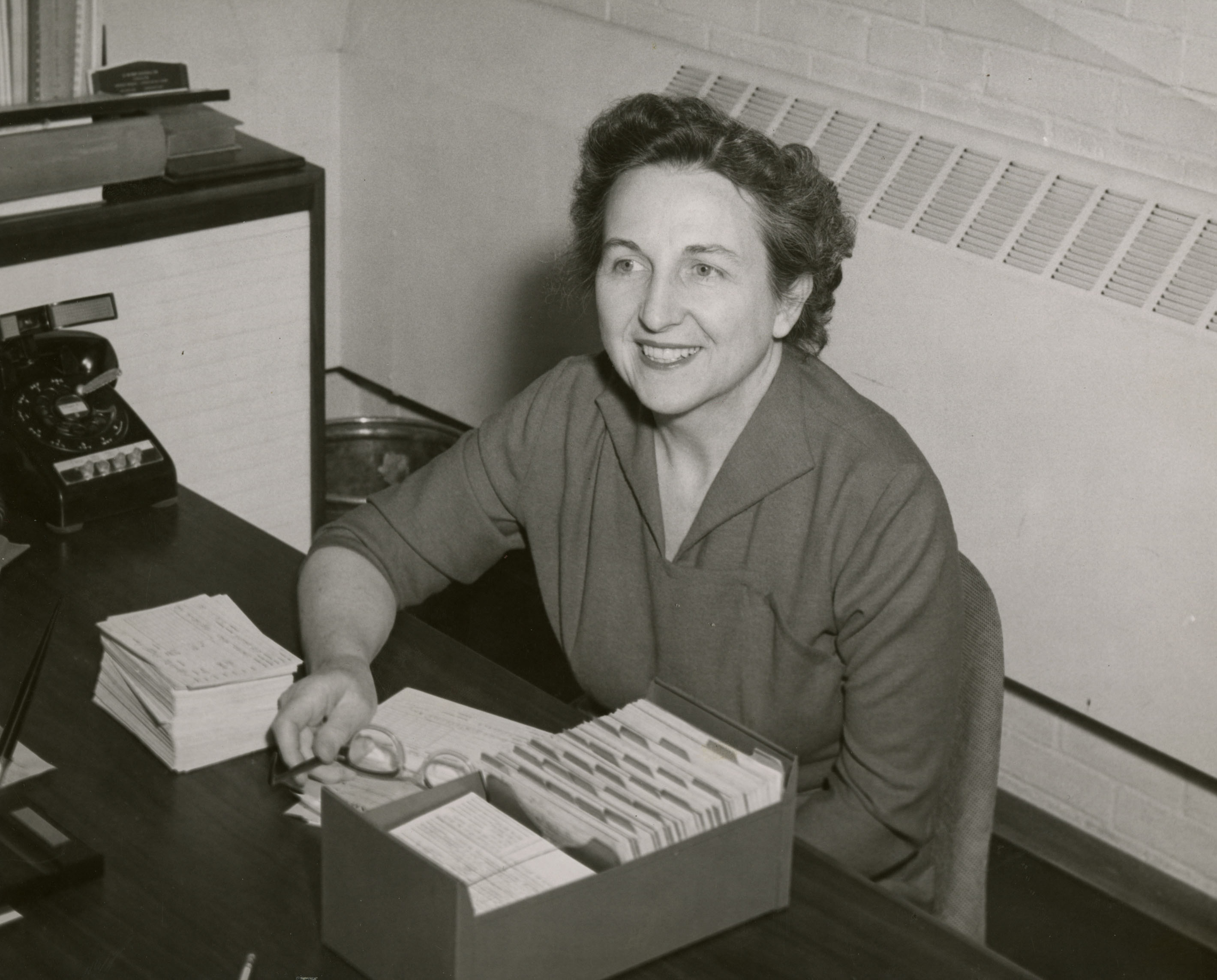 Bonnie Cone sitting at her desk, 1958